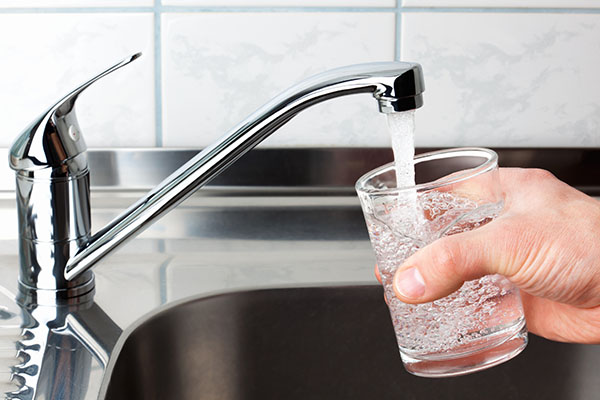 Glass filled with drinking water from kitchen faucet. Hand holding a glass of water poured from the kitchen faucet.